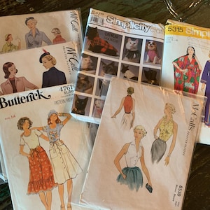 May include: A collection of vintage sewing patterns, including Butterick, McCall's, and Simplicity brands. The patterns feature illustrations of women's clothing designs, with some patterns showcasing cat and dog clothing. The patterns are in plastic sleeves.