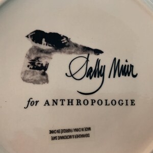 May include: White ceramic plate with a black illustration and the text "Sally Muir for ANTHROPOLOGIE". The plate is dishwasher and microwave safe, made in China.