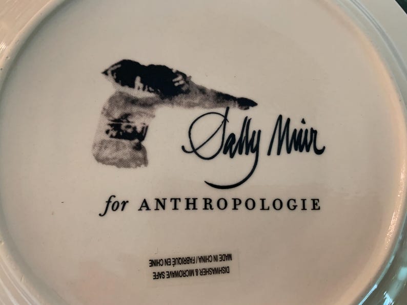 May include: White ceramic plate with a black illustration and the text "Sally Muir for ANTHROPOLOGIE". The plate is dishwasher and microwave safe, made in China.