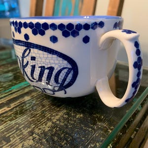 May include: A white ceramic mug with a blue and white geometric pattern and the word "Baking" written in a blue mosaic style.