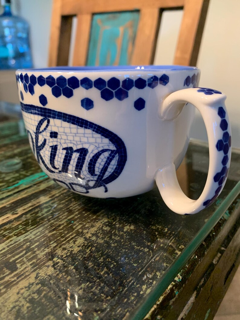 May include: A white ceramic mug with a blue and white geometric pattern and the word "Baking" written in a blue mosaic style.