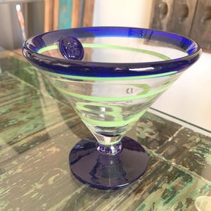 May include: A white ceramic mug with a black handle and the text "But First, Coffee" in a black, bold font. The mug is sitting on a wooden surface. The mug is 4 inches tall.