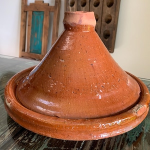 May include: A traditional, terracotta tagine pot with a conical lid and a wide, shallow base. The earthenware pot is a warm, reddish-brown color, with a slightly glossy finish. The tagine is designed for slow cooking.