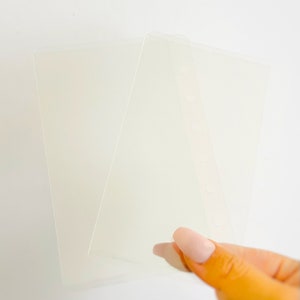 Könnte beinhalten: Transparente, durchscheinende Kunststoff-Ordner-Einsätze. Die Einsätze haben eine glatte Oberfläche und sind rechteckig mit abgerundeten Ecken. Ein Einsatz hat vorgestanzte Löcher an der Seite zum Binden.