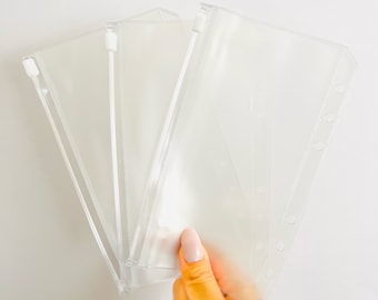May include: Three clear plastic zippered pouches with a hole punch design. The pouches are stacked on top of each other.