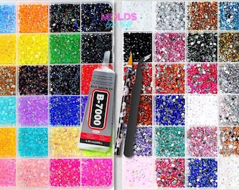 Può includere: Un contenitore a scomparti multipli riempito con piccoli strass colorati in varie tonalità tra cui blu, arancione, nero, giallo, verde, rosa e trasparente. Sono inclusi un tubetto di colla B-7000, una matita applicatrice a motivi e una pinzetta nera.