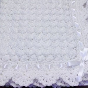 May include: A white crocheted baby blanket with a scalloped edge and white satin ribbon trim.