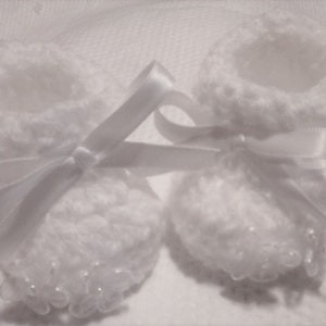 May include: Two white crocheted baby booties with white satin ribbon tied around them.