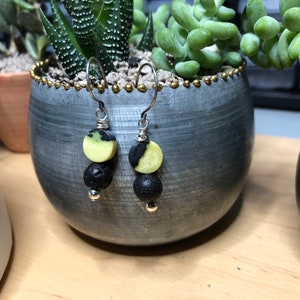 May include: A pair of earrings with black lava stone beads and yellow and black patterned round beads. The earrings are hanging from silver hooks.