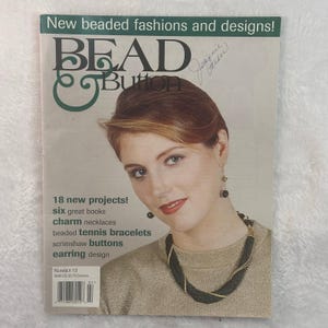 Może przedstawiać: Okładka magazynu z tytułem "BEAD & Button" przedstawiająca kobietę noszącą biżuterię z koralików. Okładka zawiera tekst o nowych projektach, naszyjnikach z zawieszkami i projekcie kolczyków. Magazyn oznaczony jest jako "Numer 13".
