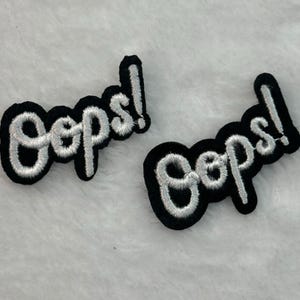 Conjunto de 2 apliques termocolantes bordados "Oops!" em preto e branco com o slogan "OS".