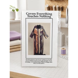 May include: A sewing pattern envelope titled Covers Everything Touches Nothing, featuring a photograph of a long, open-front garment with a dark, patterned fabric. The text describes it as a one-size pattern for a draped garment.