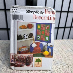 May include: A Simplicity Home Decorating pattern packet featuring sports-themed designs. The packet includes images of a football, basketball, soccer ball, and a quilt with sports ball designs. The packet also shows a beanbag chair and other decorative items.