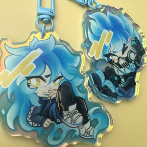 Puede incluir: Dos llaveros acr&iacute;licos con personajes de estilo anime con cabello y atuendos azules. Los llaveros tienen un efecto hologr&aacute;fico y est&aacute;n unidos a cierres azul claro. Un personaje est&aacute; sentado, el otro en una pose din&aacute;mica.