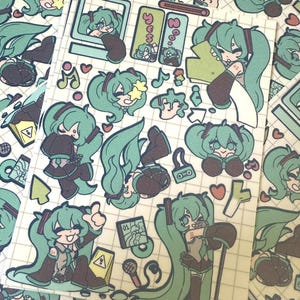 May include: Sheet of stickers featuring a teal-haired anime character in various poses. The stickers include musical notes, hearts, and computer-related graphics. The background is a grid pattern.
