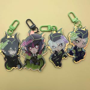 Puede incluir: Cuatro llaveros de personajes con detalles en verde y negro. Cada llavero presenta un personaje de estilo anime diferente con cabello y ropa &uacute;nicos. Los llaveros tienen cierres verdes o negros.