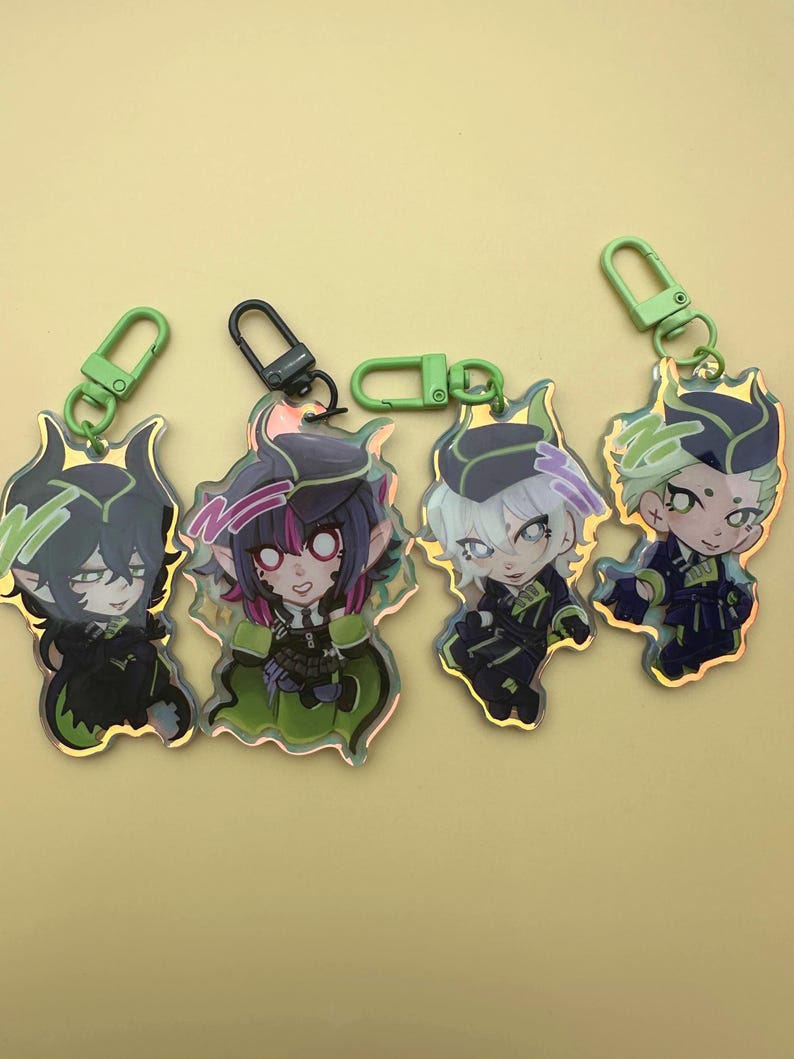 Puede incluir: Cuatro llaveros de personajes con detalles en verde y negro. Cada llavero presenta un personaje de estilo anime diferente con cabello y ropa &uacute;nicos. Los llaveros tienen cierres verdes o negros.