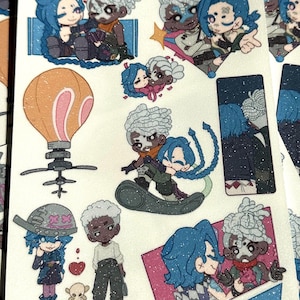 May include: A sheet of glittery stickers featuring cartoon illustrations of characters with blue and white hair. The stickers depict various poses, including hugging and standing. A large orange hot air balloon sticker is also visible.