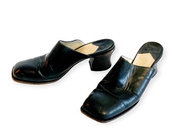 May include: A pair of black leather clogs with square toes and block heels. The open-back shoes have a slip-on design and a neutral-colored insole. The heels are approximately 2 inches high.