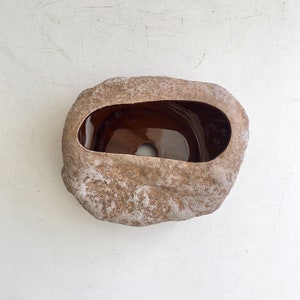 May include: A brown ceramic planter shaped like a rock with a brown glazed interior. The planter has a rough, textured surface and a hole in the bottom for drainage.