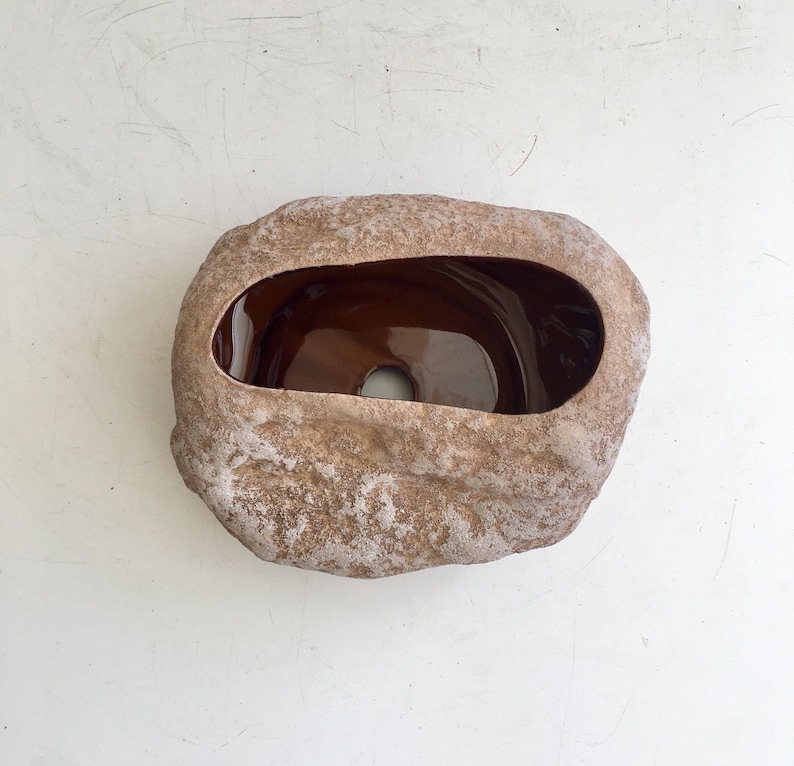 May include: A brown ceramic planter shaped like a rock with a brown glazed interior. The planter has a rough, textured surface and a hole in the bottom for drainage.