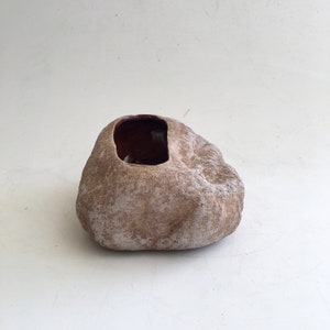 May include: A brown ceramic planter shaped like a rock with a rectangular opening for planting. The planter has a rough, textured surface.