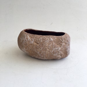 May include: A light brown ceramic planter shaped like a rock with a dark brown interior.