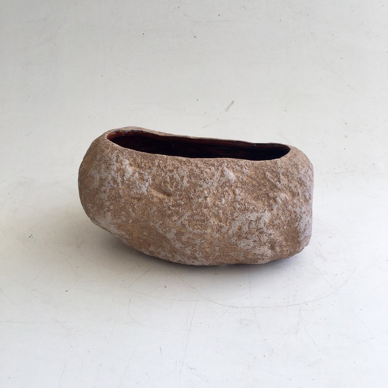 May include: A light brown ceramic planter shaped like a rock with a dark brown interior.