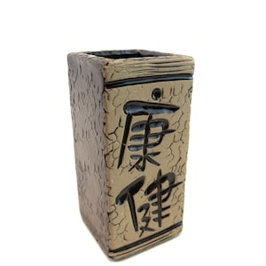 May include: A rectangular ceramic vase with a textured, cracked surface in shades of brown and tan. Black Chinese characters are carved into the front. The top edge has a dark brown band.
