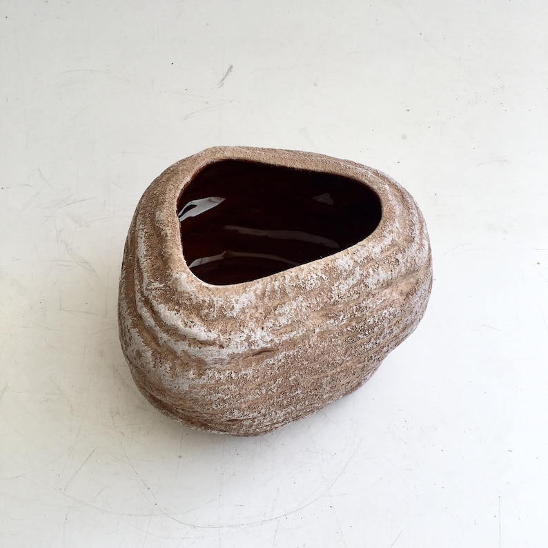May include: A brown and white ceramic planter with a textured, stone-like appearance. The interior is a dark brown color. The oval-shaped opening is at the top. The planter is suitable for indoor or outdoor use.