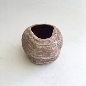 May include: A small, textured, brown and white ceramic pot with a dark interior. The pot has a unique, organic shape with a wide opening. The exterior features a layered, ridged design, creating a rustic appearance. Ideal for small plants or decorative use.