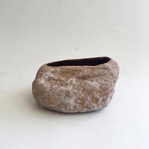 May include: A brown ceramic planter shaped like a rock with a rough, textured surface. The planter has a brown glazed interior.