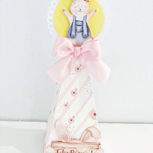 May include: A pink and white cone-shaped party favor with a bunny rabbit illustration and the text "Feliz Pascoa!"  The cone has a pink bow and a yellow circle with a bunny rabbit illustration on top.