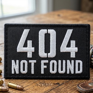May include: Black rectangular patch with white embroidered text reading "404 NOT FOUND." The patch is on a wooden surface with several bullets and a leather item in the background. The text is in a bold, sans-serif font.