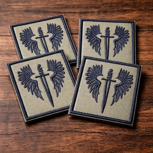 May include: Four square patches with a dark blue embroidered design of a sword with wings on a tan background. Each patch has a dark blue border. The patches are arranged on a wooden surface.