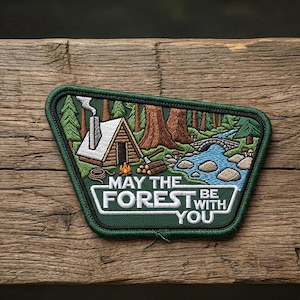 May include: Embroidered patch with a forest scene, featuring a cabin, river, and bridge. The patch has a green border and the text "MAY THE FOREST BE WITH YOU" in white.