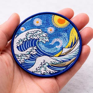 May include: Round embroidered patch featuring a stylized depiction of a wave and starry night sky. The design incorporates shades of blue, white, yellow, and orange. The patch has a blue border and is held in a hand.