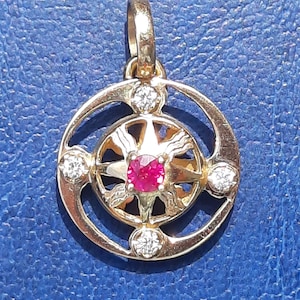 Peut inclure: Un pendentif en or avec un rubis rouge au centre et quatre petits diamants autour. Le pendentif est en forme d'étoile avec un cadre circulaire.