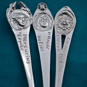 May include: Three silver spoons with decorative handles featuring Greek mythological figures. The spoons are engraved with the names "Mercury", "Helios", and "Gorgon Medusa".