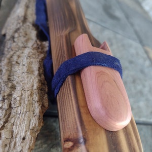 May include: A wooden flute with a dark brown finish and a natural wood mouthpiece. The flute is wrapped with a dark blue strap and has a small, round, light brown wooden plug on the end.
