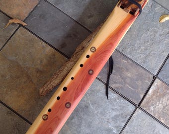 May include: A wooden flute with a natural wood finish and decorative inlays. The flute has a black leather strap and a turquoise stone inlay.