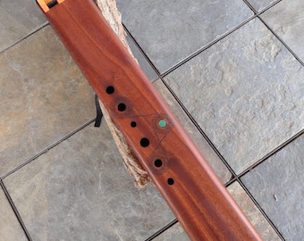 May include: A wooden flute with a dark red finish and a purple accent at the end. The flute has a series of holes along the top and a decorative design with a green stone.