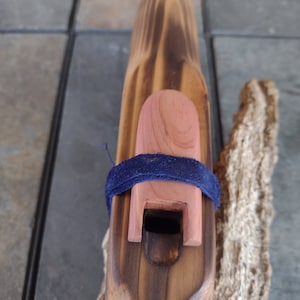 May include: A wooden flute with a dark brown stain and a natural wood mouthpiece. The flute is decorated with a blue ribbon and a red wooden cap.