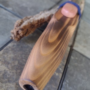 May include: A wooden flute with a brown stain and a natural wood finish. The flute has a small hole at the end and a blue string wrapped around the top.