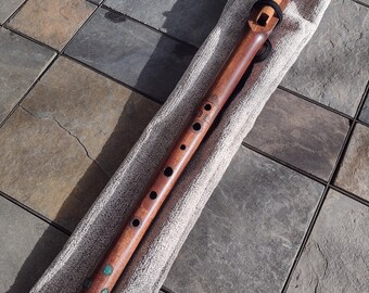 May include: A wooden flute with turquoise accents, lying in a gray fabric bag. The flute has six holes and a mouthpiece.