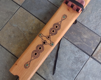 May include: A wooden flute with a decorative design featuring circles and turquoise accents. The flute has a black leather strap and a mouthpiece made of a different type of wood.