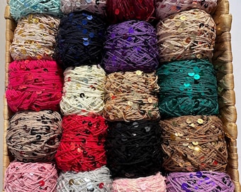 May include: A woven basket filled with various colorful yarn balls. The yarn is in shades of teal, pink, red, black, and brown, with sequins. The basket has a brown handle. The yarn is suitable for knitting and crochet projects.