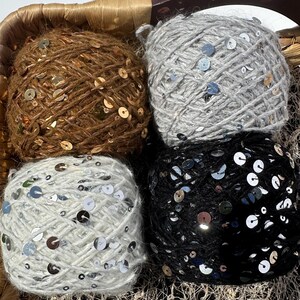 Può includere: Quattro gomitoli di lana con paillettes, in marrone, grigio, bianco e nero.