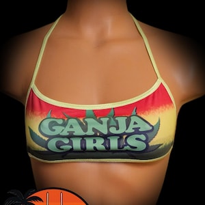 May include: A halter-style bikini top with a colorful design. The top features the text "GANJA GIRLS" in green, set against a background of red, yellow, and green, with a light green trim. The Pixiehemp Bikini Hut logo is in the lower left.