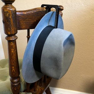 May include: A gray fedora hat with a black band hanging on a wooden chair with a black metal hook.
